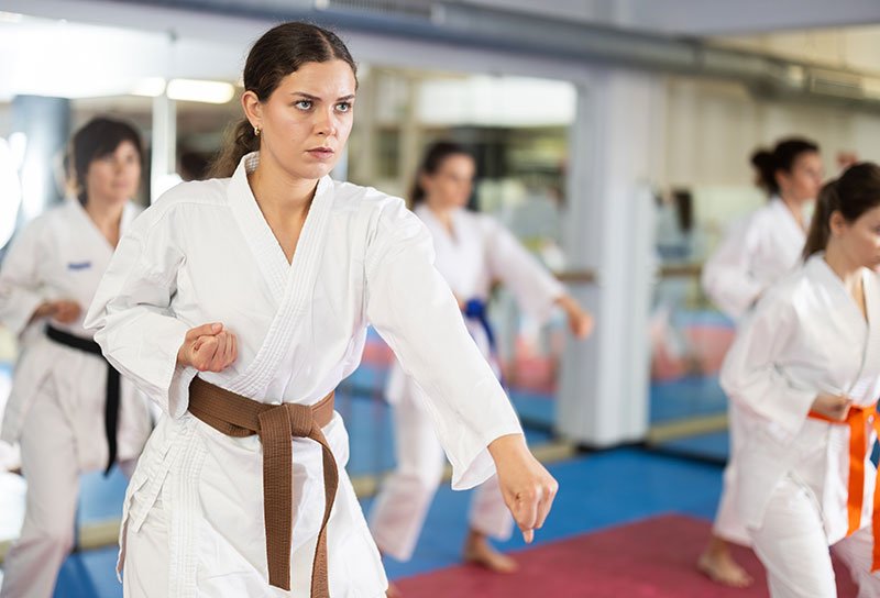 A female martial artist with a brown belt executing a punch in a training dojo.