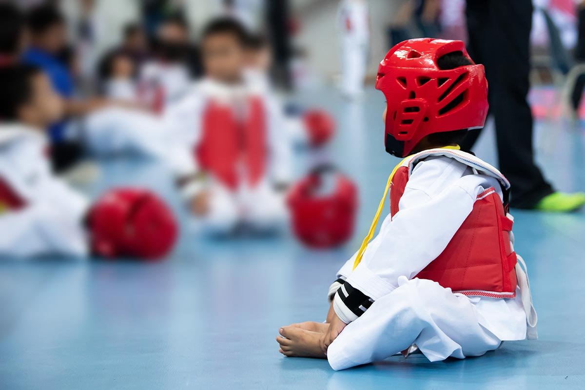 Young child wearing Taekwondo protective gear sitting on a padded mat during kids martial arts class